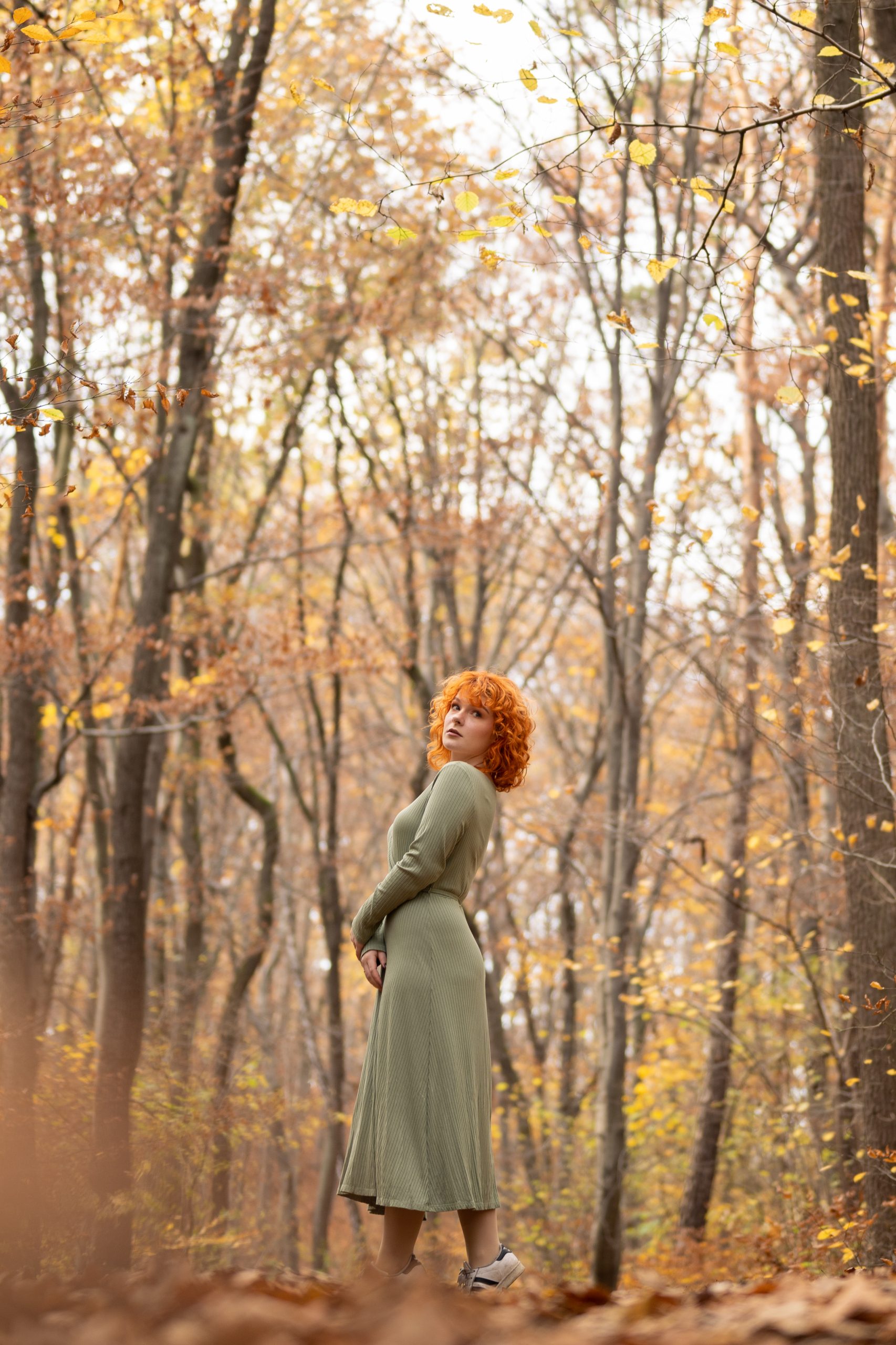 Ruda dziewczyna stoi na ścieżce leśnej, w tle drzewa w jesiennych kolorach